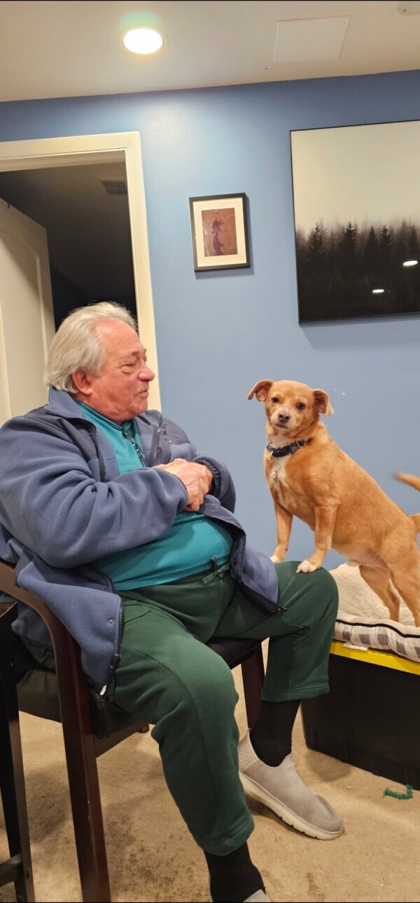 An older man sitting on a chair with a dog.